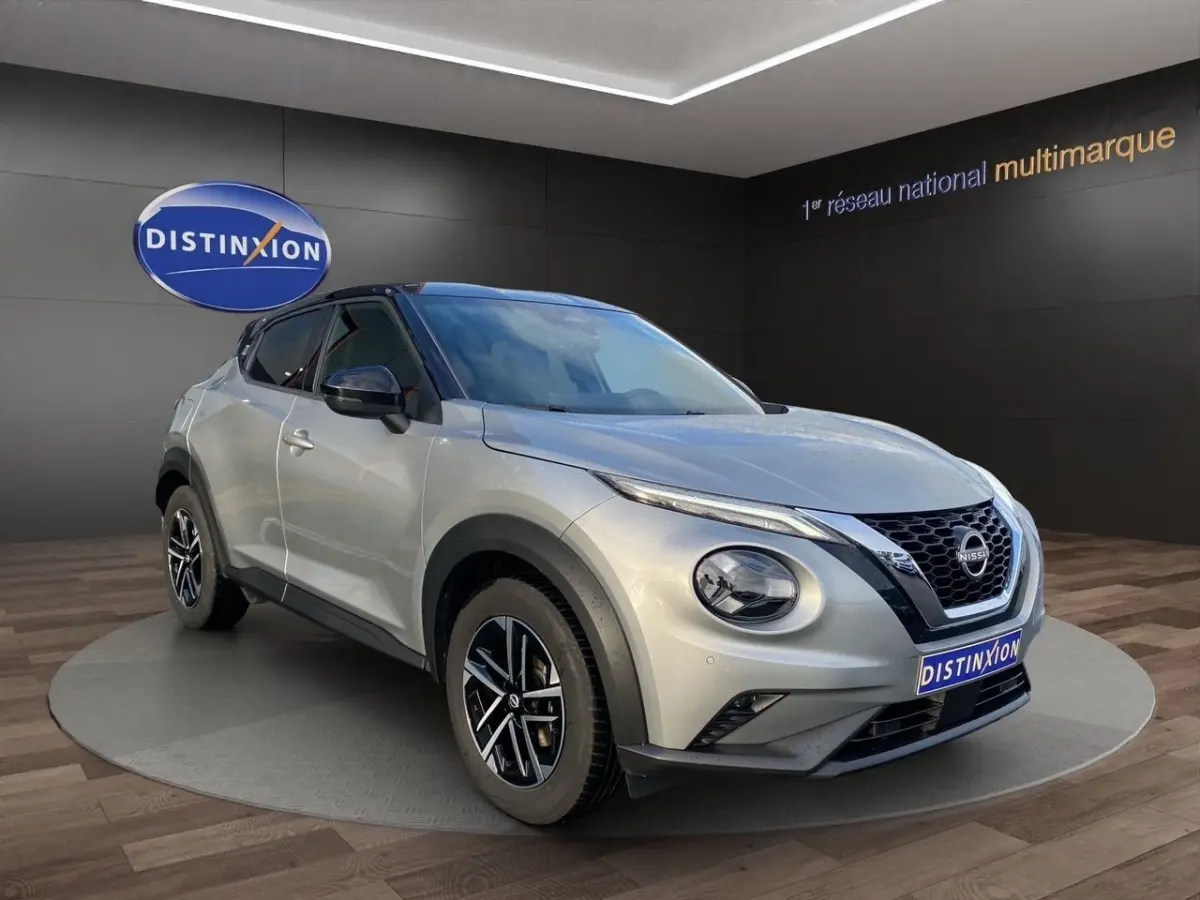 Nissan Juke gris clair vu en 3/4 avant droit, avec toit noir et jantes alliage distinctives.
