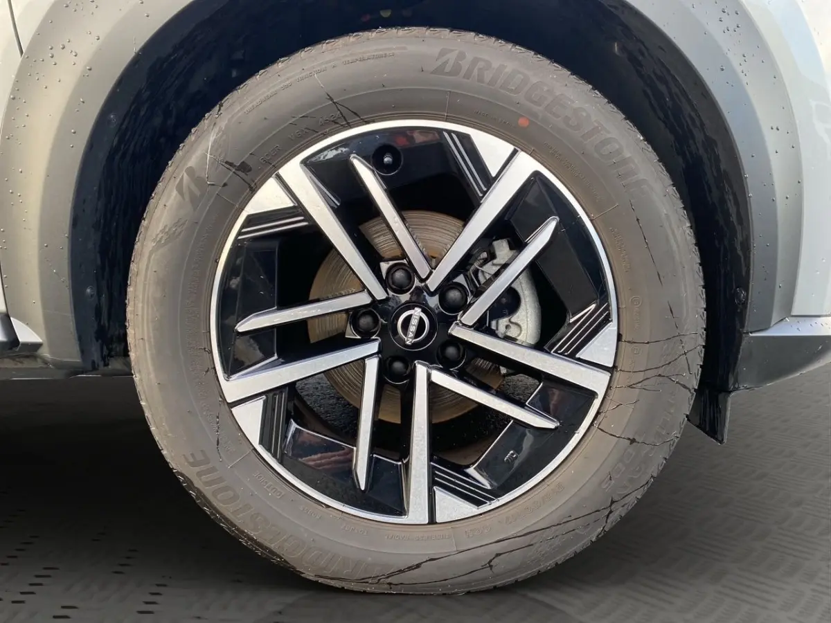 Gros plan sur la roue avant droite du Nissan Juke gris clair, mettant en valeur la jante alliage noire et argentée.