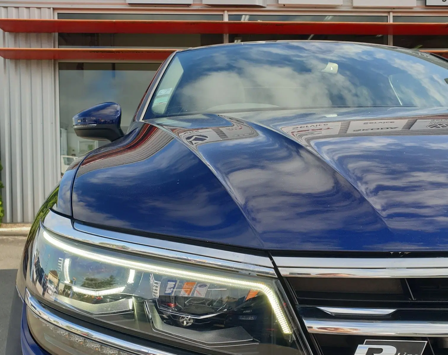 Gros plan sur l'avant gauche d'un Volkswagen Tiguan bleu Atlantique métallisé avec badge R-Line et phares LED allumés.