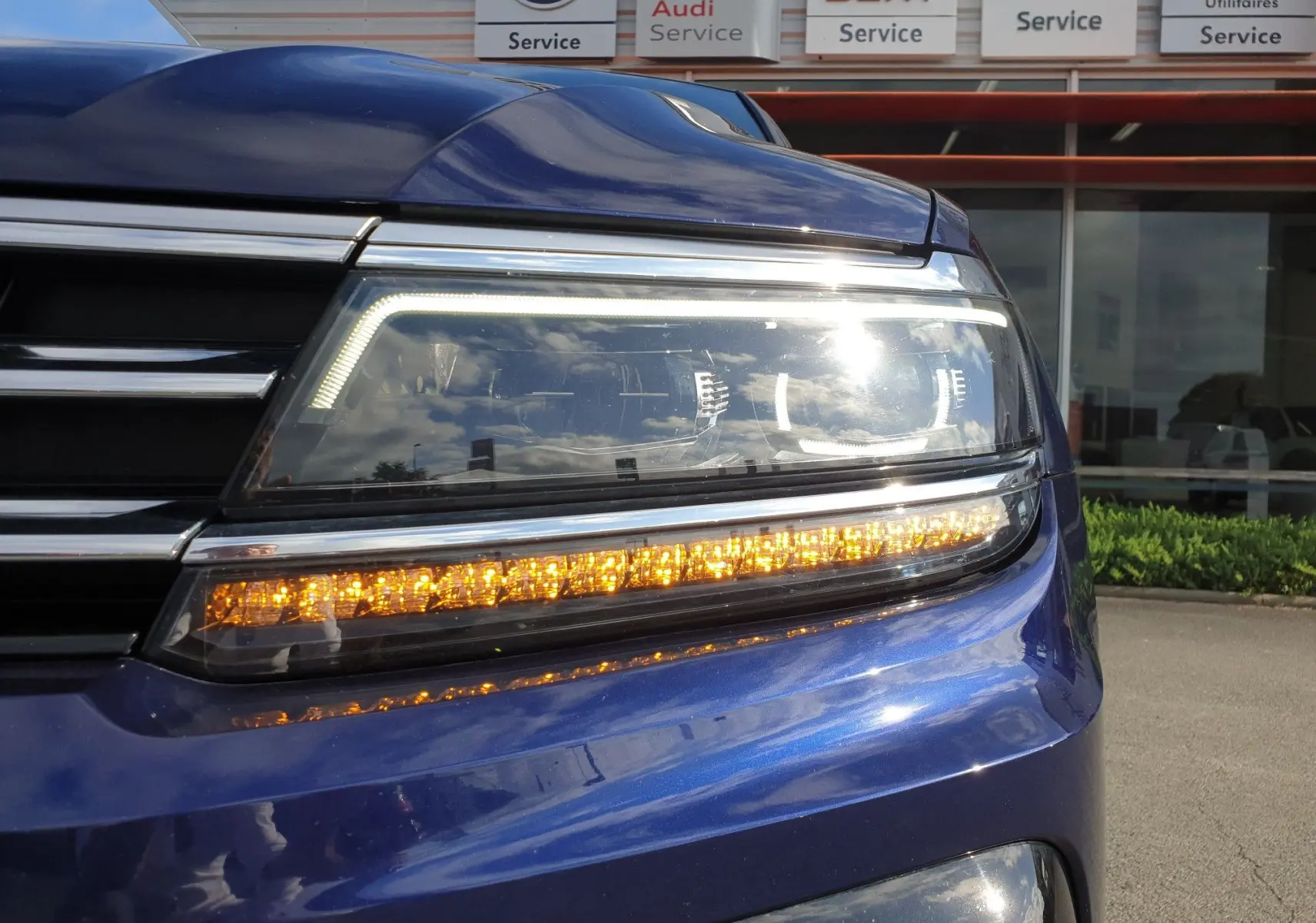Gros plan sur le phare avant droit bleu Atlantique métallisé d'un Volkswagen Tiguan 2018 avec clignotant allumé.