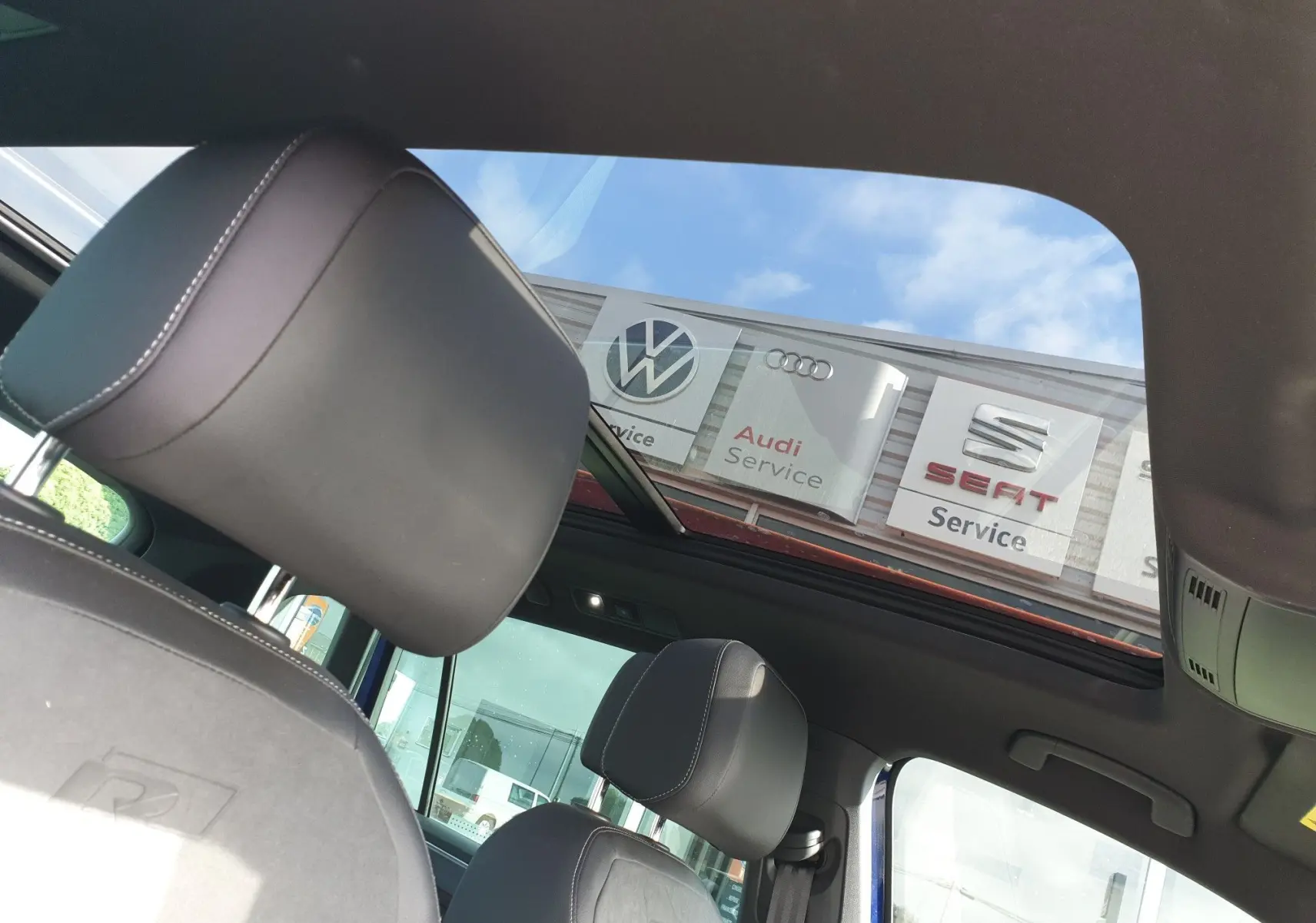 Intérieur du Volkswagen Tiguan bleu Atlantique, vue sur les sièges avant avec toit ouvrant panoramique et ciel dégagé.