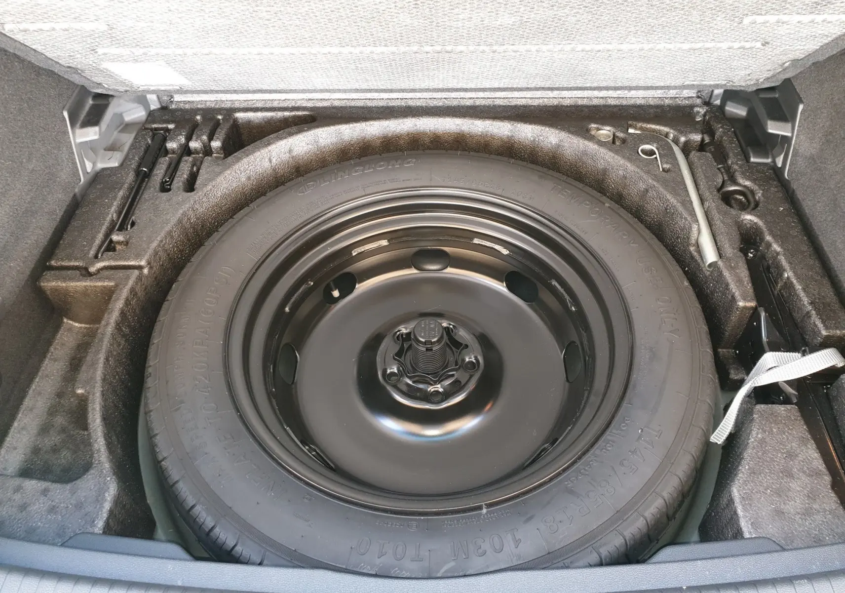 Roue de secours noire dans le coffre d'un Volkswagen Tiguan 2018, vue plongeante sur le pneu de secours.