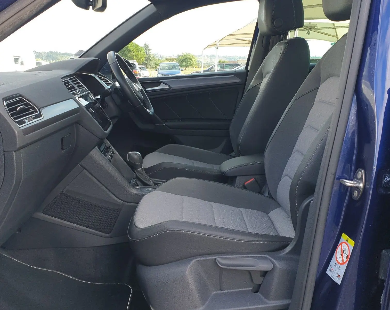Intérieur côté conducteur d'un Volkswagen Tiguan bleu Atlantique 2018, sièges tissu gris et toit ouvrant panoramique visible.