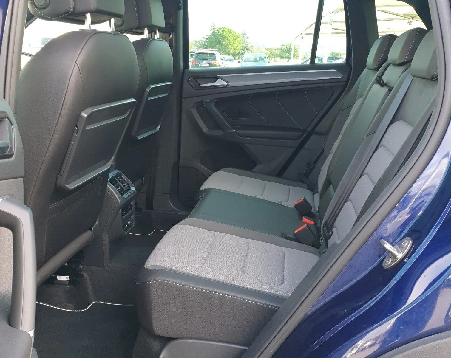 Vue intérieure côté arrière gauche du Volkswagen Tiguan bleu Atlantique, montrant les sièges arrière et le toit ouvrant panoramique.