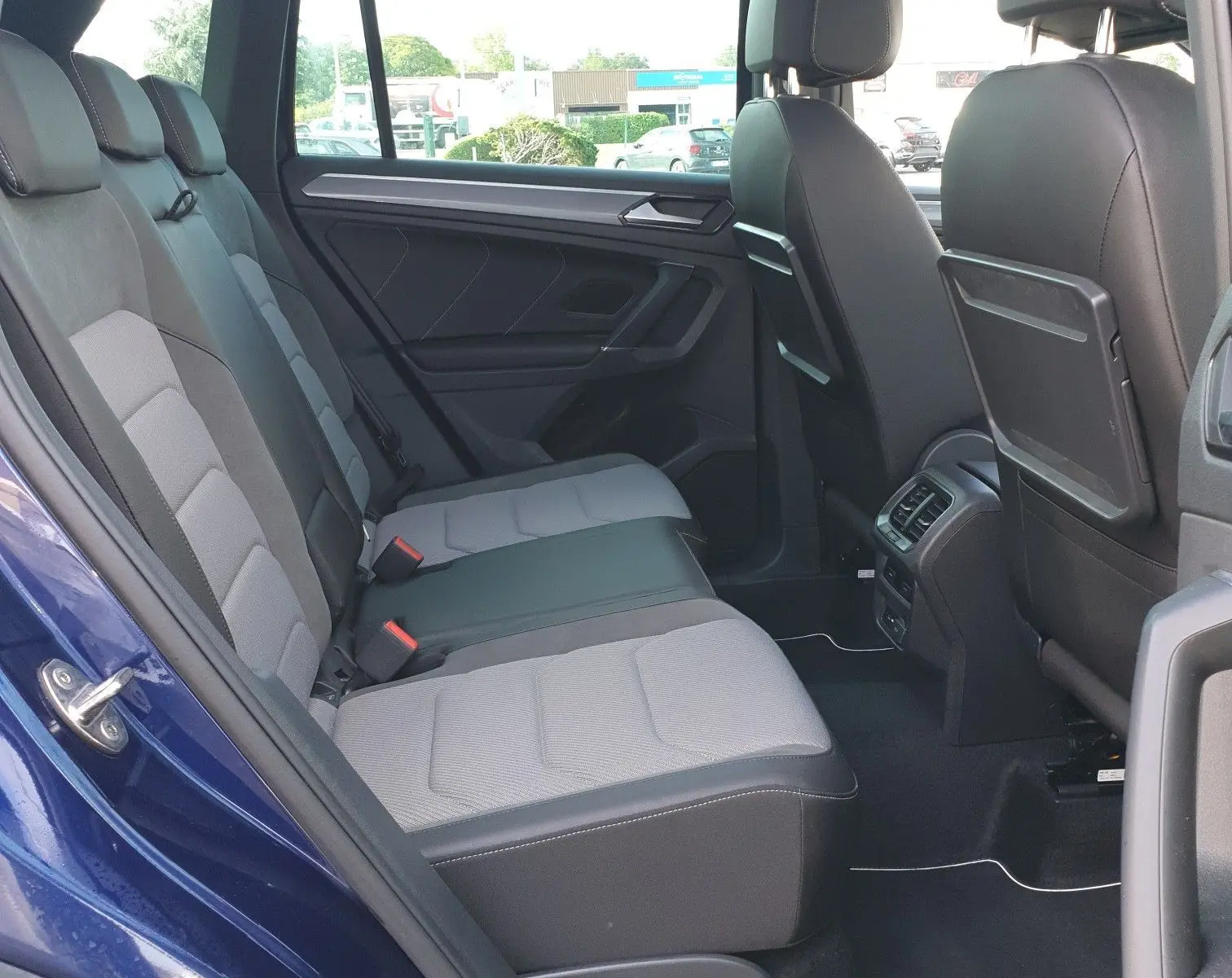 Vue intérieure arrière droite du Volkswagen Tiguan bleu Atlantique, montrant les sièges arrière et le toit ouvrant panoramique.
