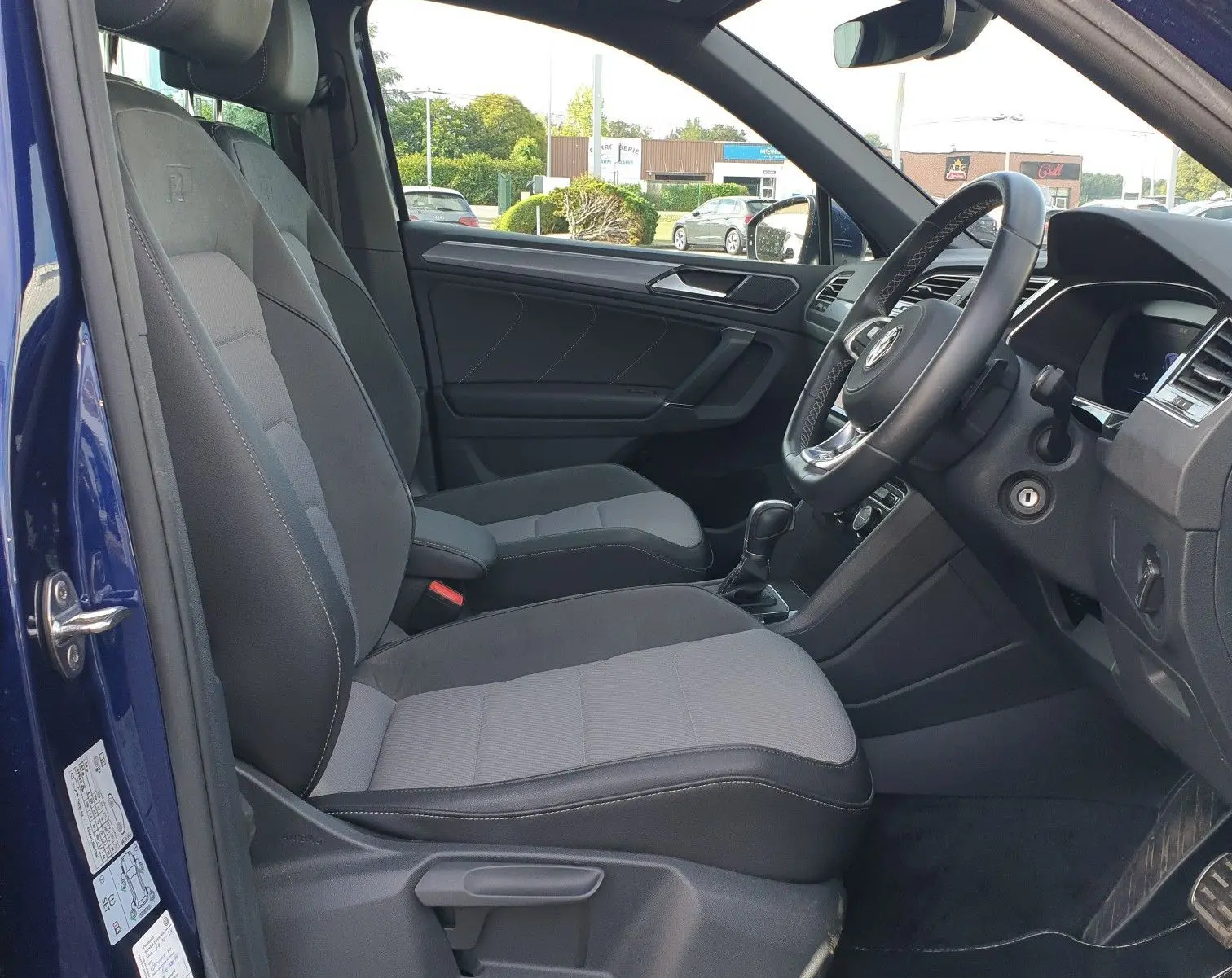 Vue intérieure côté conducteur d'un Volkswagen Tiguan bleu Atlantique avec sièges gris et volant à droite.