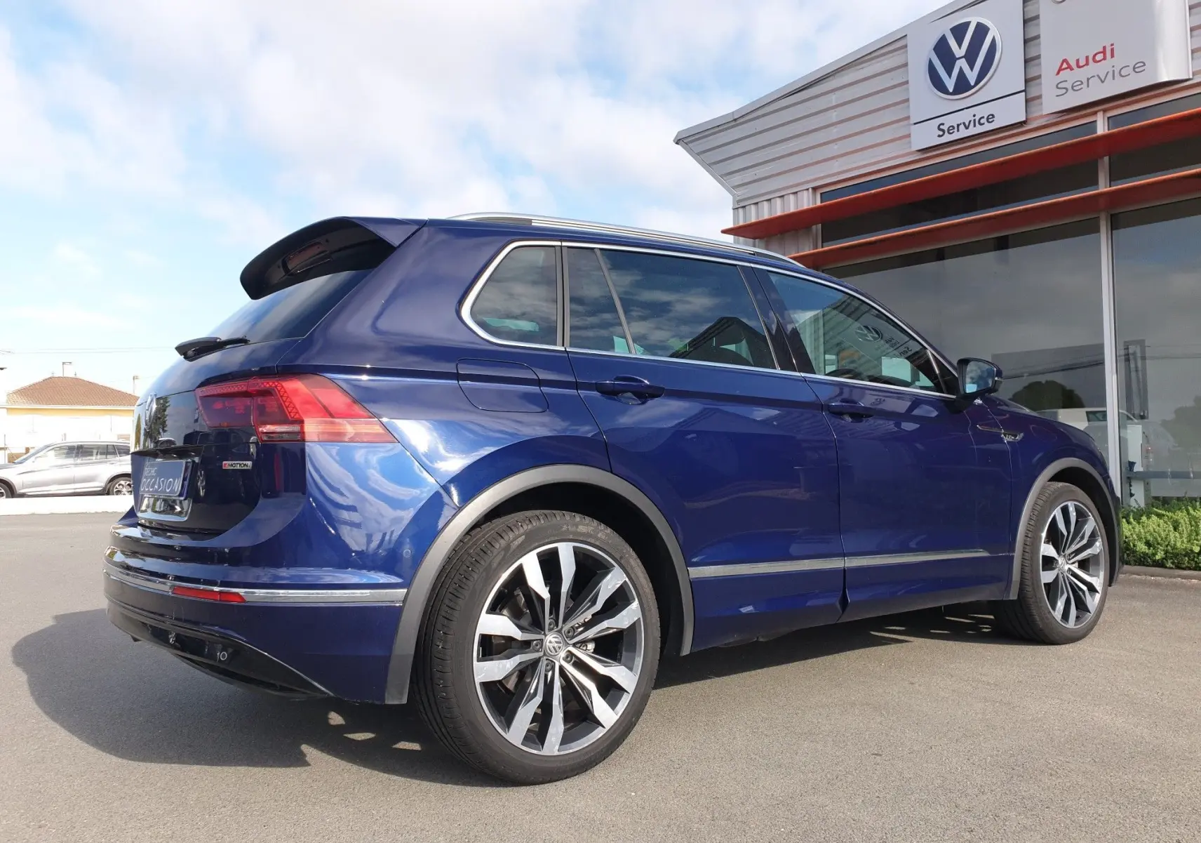 Volkswagen Tiguan bleu Atlantique métallisé vu en 3/4 arrière droit devant un service Volkswagen et Audi.