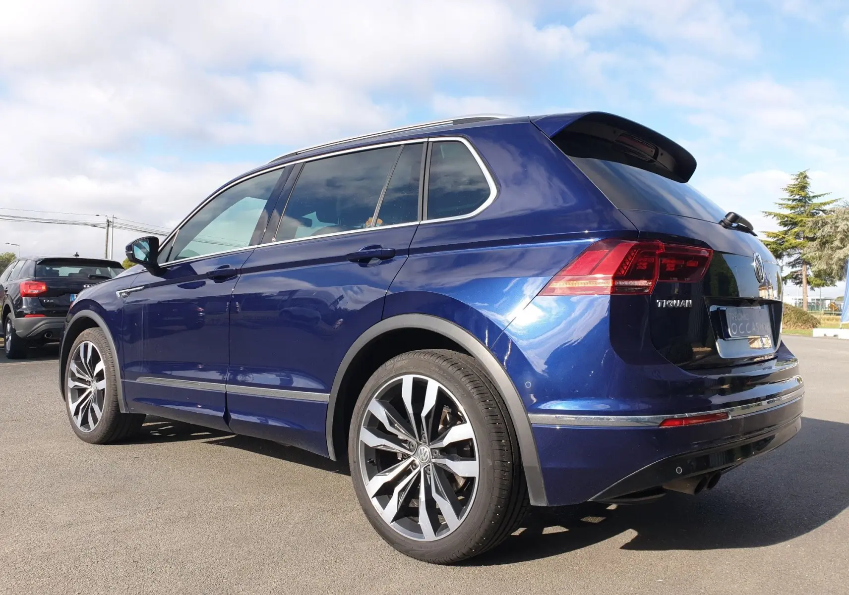 Volkswagen Tiguan bleu Atlantique métallisé vu en 3/4 arrière droit, avec jantes alliage distinctives et toit ouvrant.