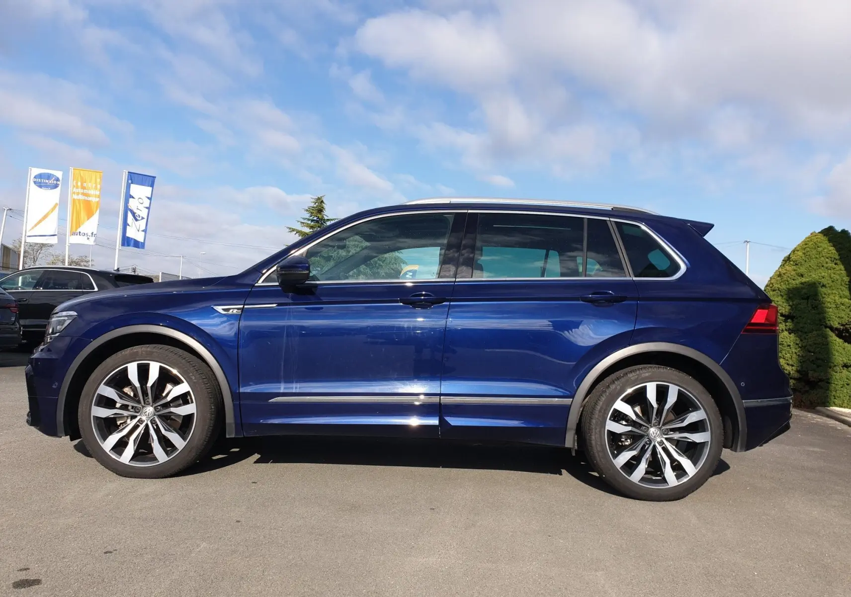 Profil côté gauche d'un Volkswagen Tiguan bleu Atlantique métallisé avec jantes alliage et toit ouvrant visible.