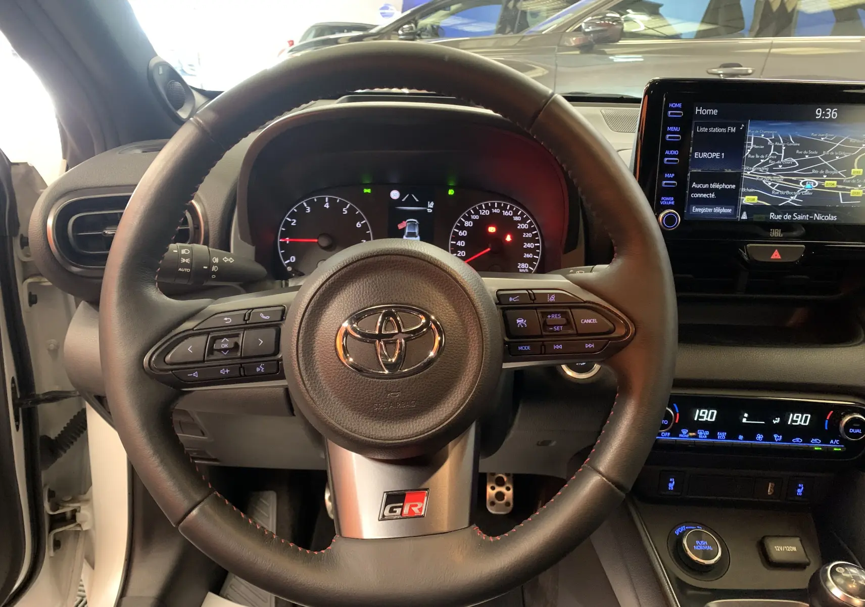 Vue intérieure centrée sur le volant cuir noir avec logo GR de la Toyota Yaris 1.6 VVT-I blanc métal.