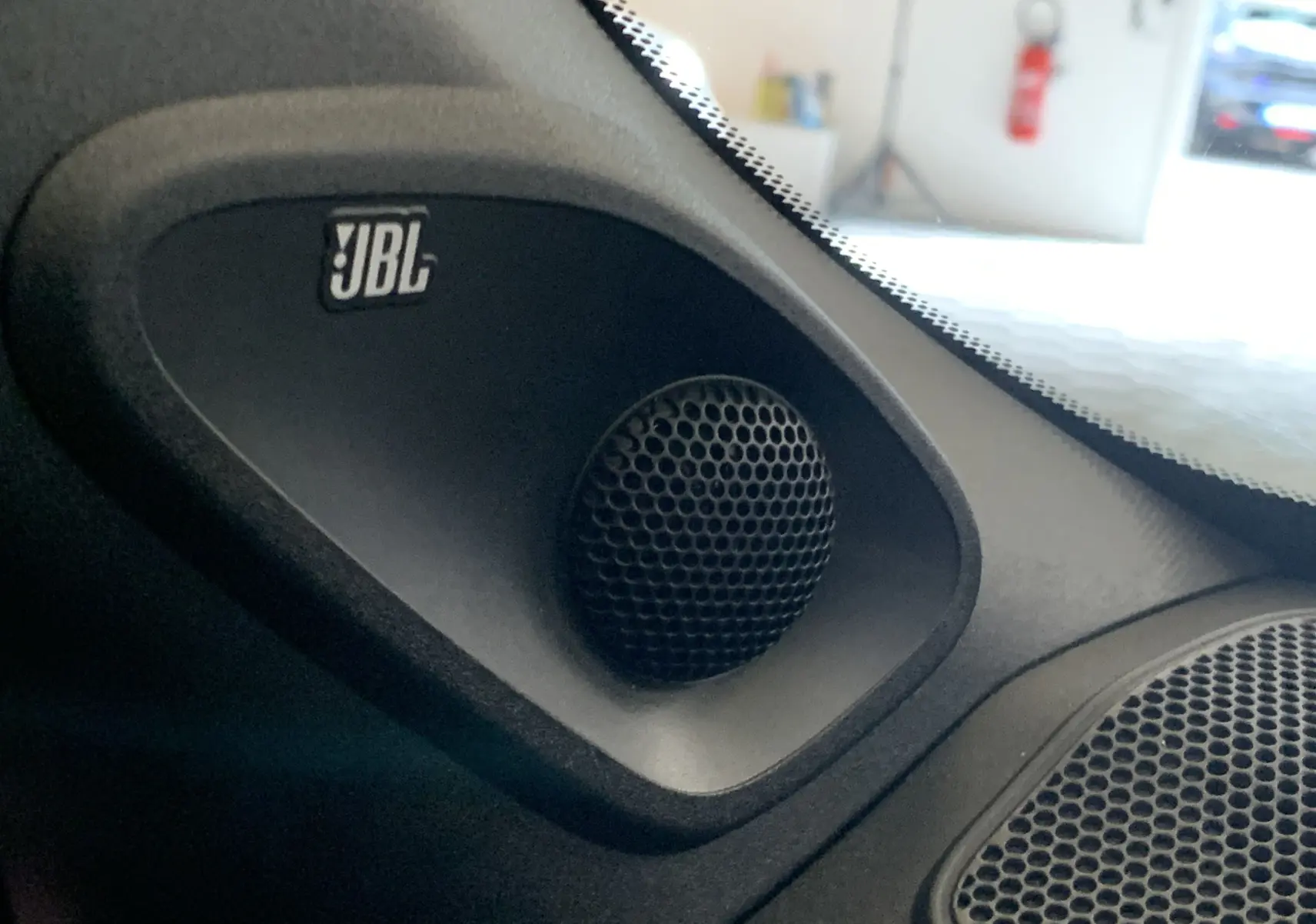 Gros plan sur le haut-parleur JBL intégré côté gauche du tableau de bord d'une Toyota Yaris blanche.