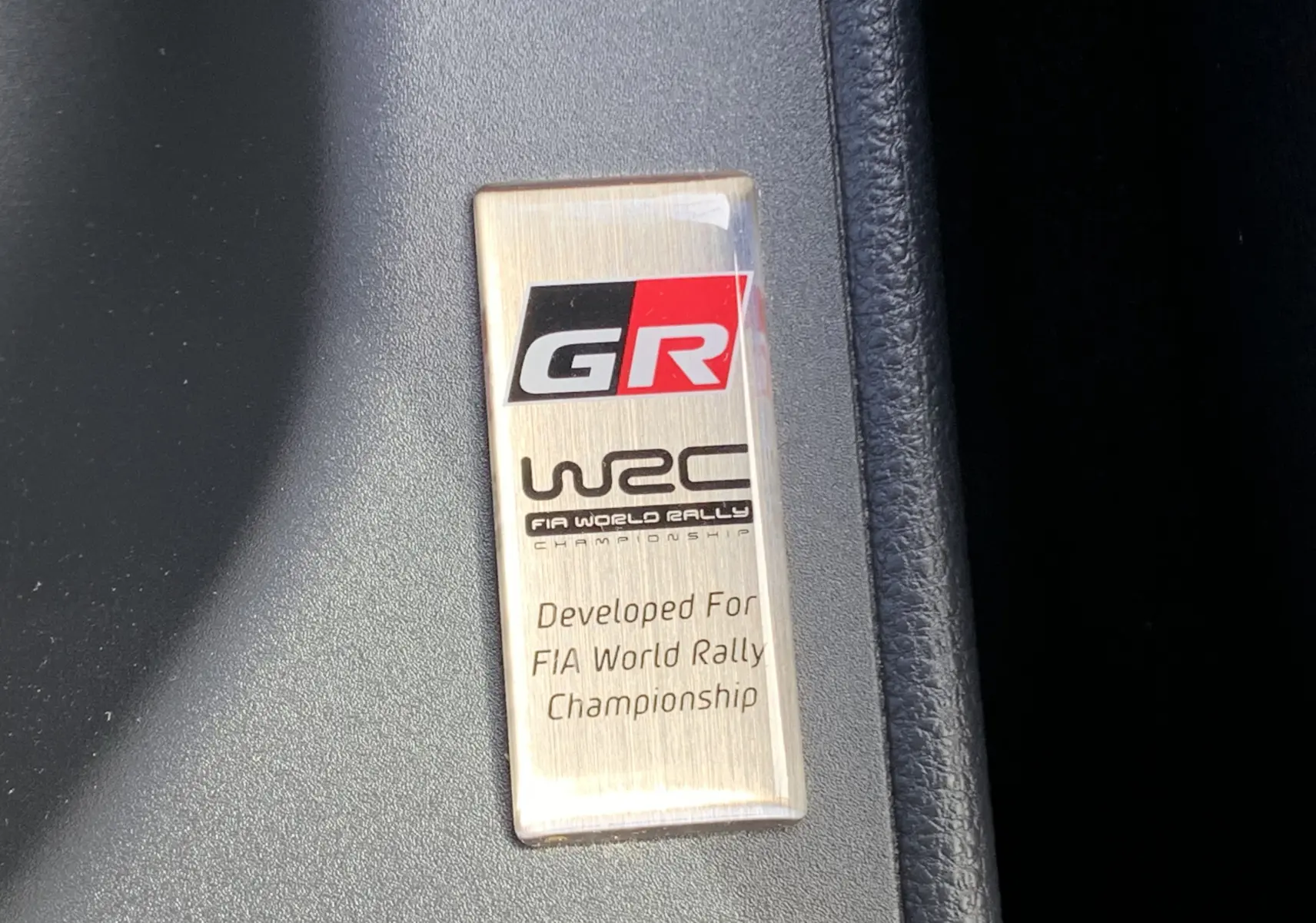 Plaque intérieure GR WRC en métal brossé sur fond noir, soulignant la version sportive Toyota Yaris 1.6 VVT-I 261 Premium.