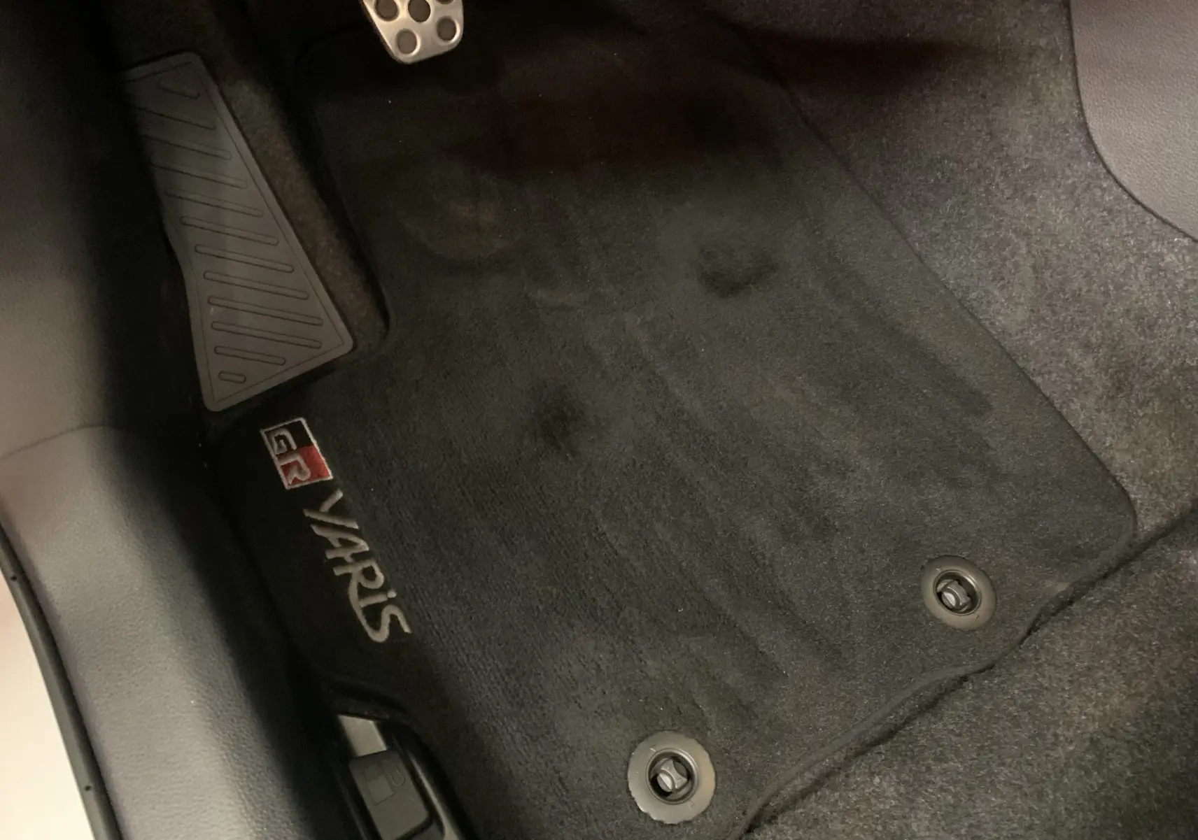 Gros plan sur le tapis de sol noir côté conducteur avec logo GR Yaris visible sur un véhicule blanc.