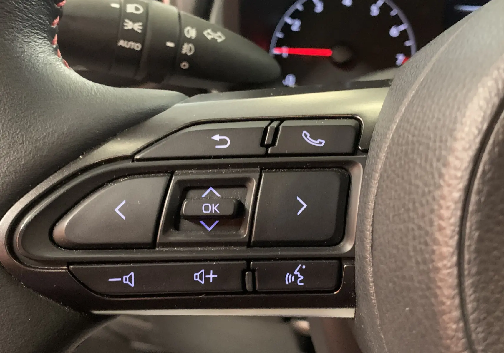 Gros plan sur les commandes au volant côté gauche de la Toyota Yaris blanche, avec boutons de navigation et téléphone.