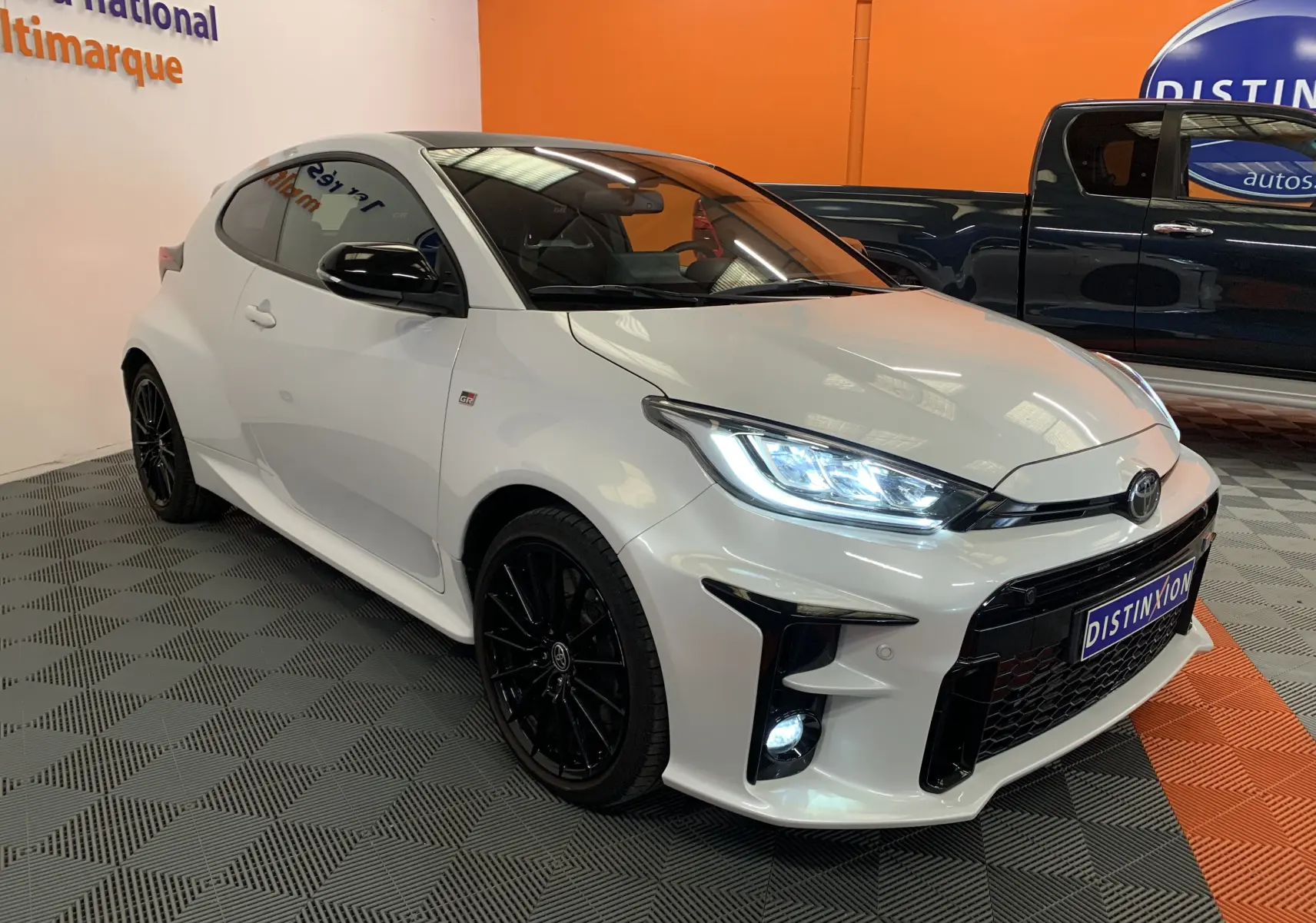 Toyota Yaris 1.6 VVT-I 261 Premium GR blanc métal vue 3/4 avant avec phares LED allumés et jantes noires.