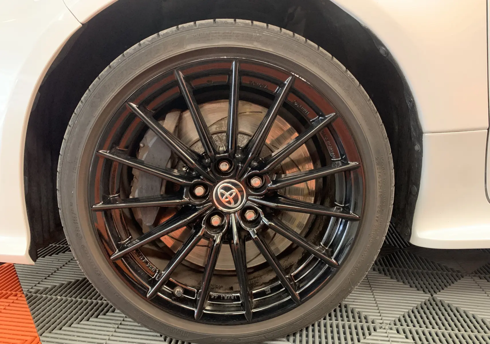 Gros plan sur la roue avant droite d'une Toyota Yaris blanche métal avec jante alliage noire multi-branches.