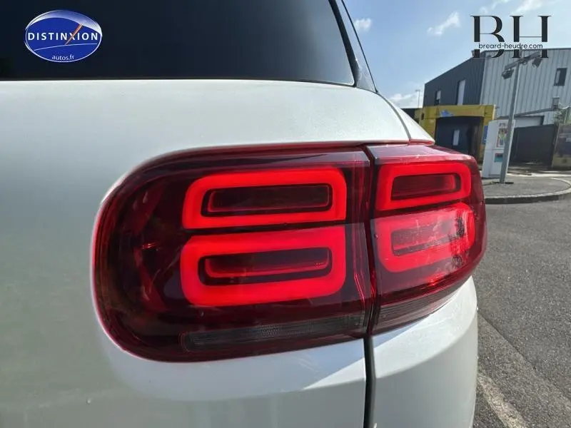 Gros plan sur le feu arrière droit rouge d'un Citroën C5 Aircross blanc nacré, avec attelage visible.