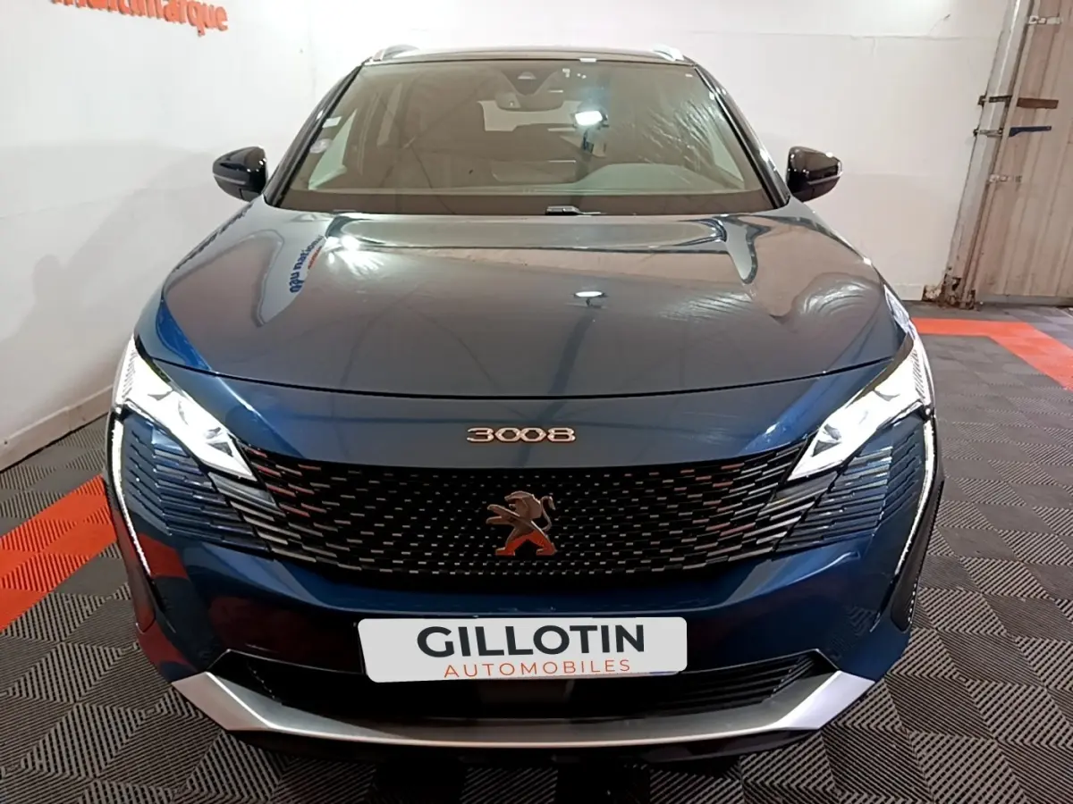 Vue avant d'un Peugeot 3008 bleu métallisé avec calandre noire et phares LED allumés en intérieur showroom.
