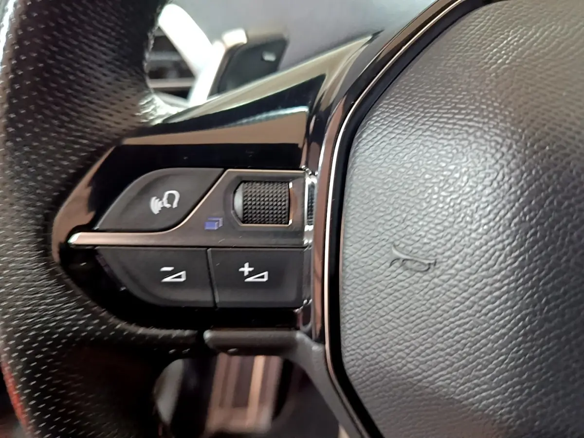 Gros plan sur les commandes gauche du volant cuir noir du Peugeot 3008 GT bleu, avec molette et boutons multifonctions.
