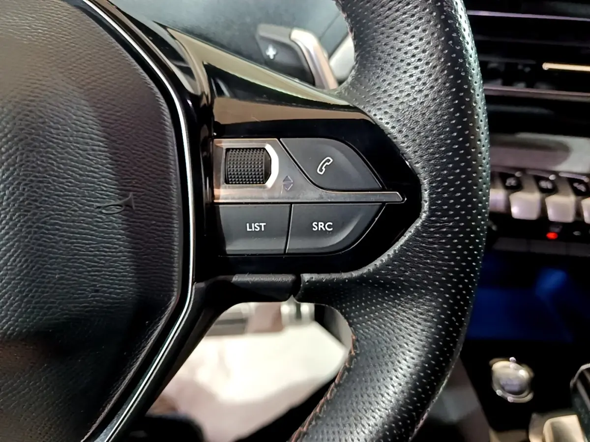 Gros plan sur le volant cuir noir perforé du Peugeot 3008 GT 2021, avec commandes multifonctions visibles.