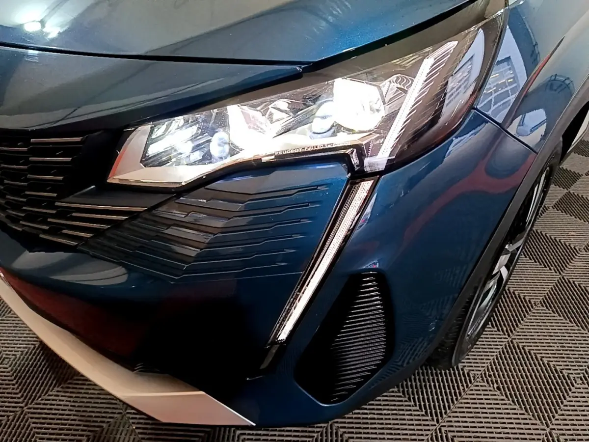 Gros plan sur l'avant droit bleu du Peugeot 3008 2021, mettant en valeur le phare LED et la calandre stylisée.