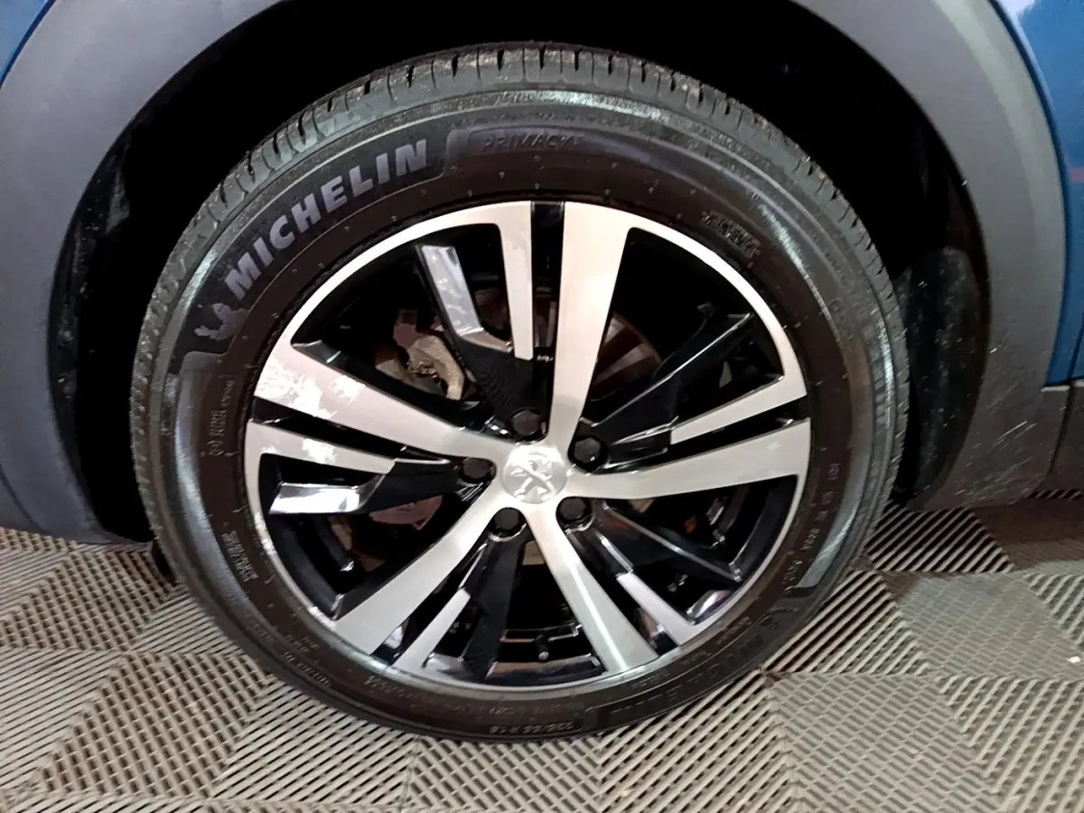 Gros plan sur la roue avant gauche du Peugeot 3008 bleu, avec jante alliage bicolore et pneu Michelin.