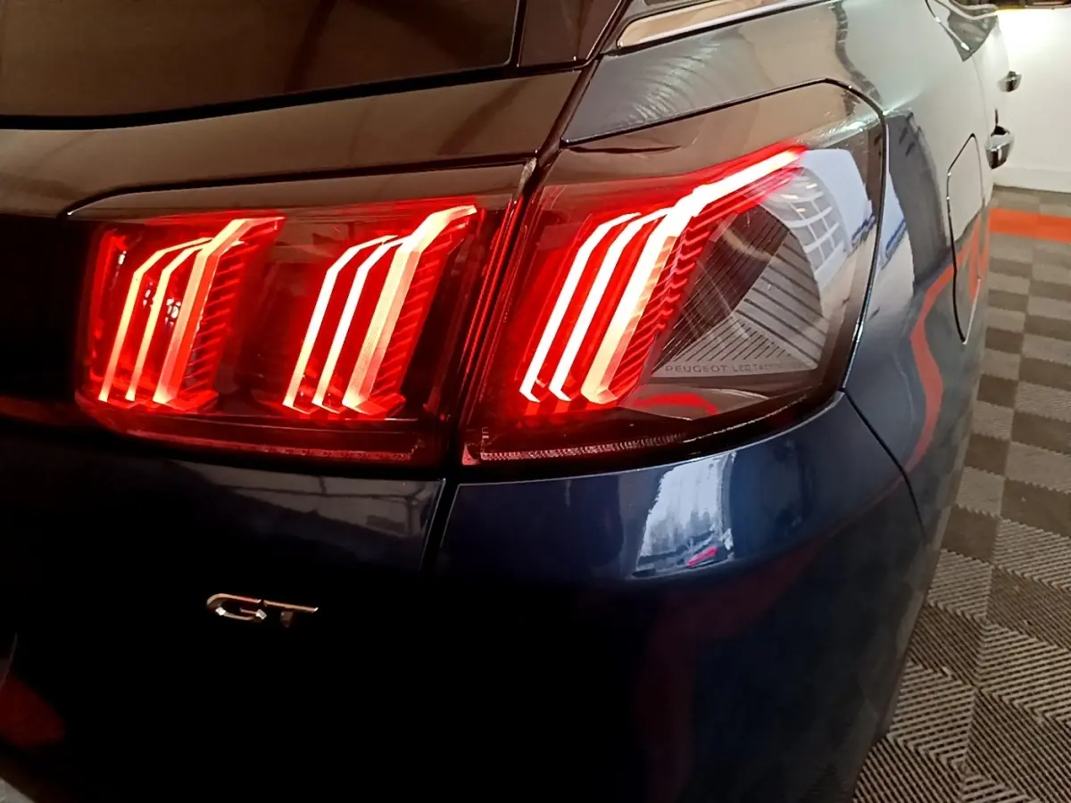 Gros plan sur le feu arrière droit allumé d’un Peugeot 3008 GT bleu, avec logo GT visible sur la carrosserie.