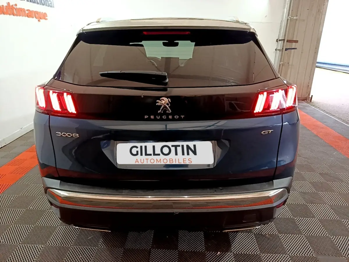 Vue arrière d'un Peugeot 3008 GT bleu avec feux LED allumés et bandeau noir brillant sur le hayon.