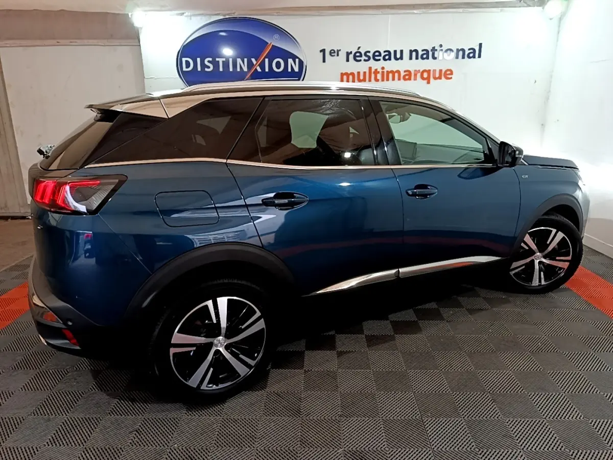 Vue côté droit du Peugeot 3008 PureTech 130 GT bleu, avec jantes alliage et toit noir contrasté en intérieur showroom.