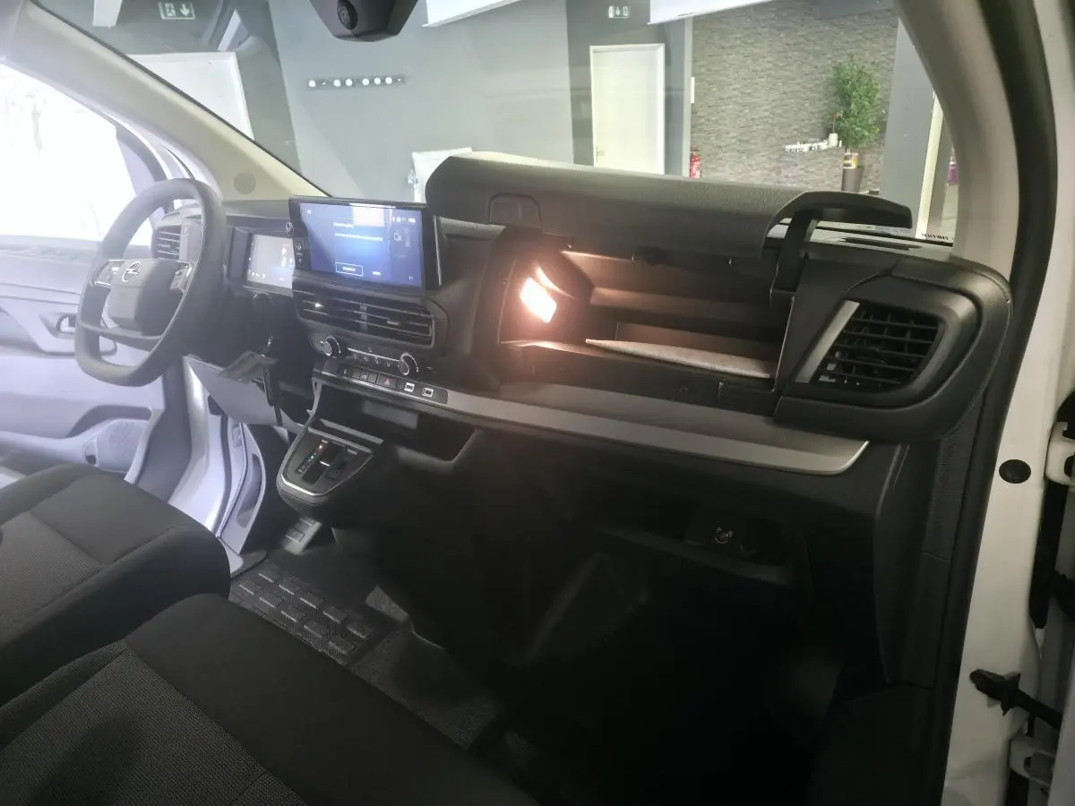 Vue intérieure côté passager de l'Opel Vivaro blanc 2025, tableau de bord avec écran tactile et boîte à gants ouverte éclairée.