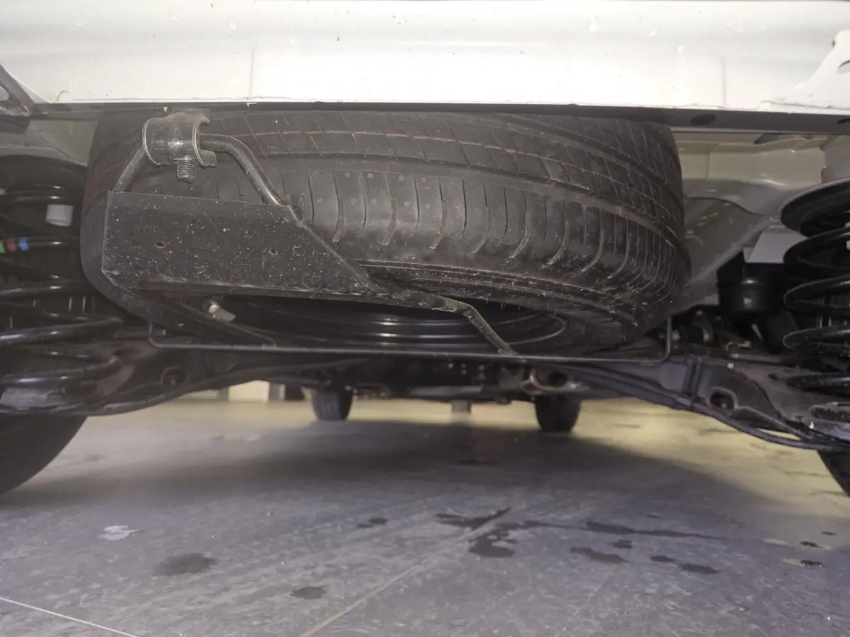 Vue en contre-plongée sous l'arrière d'un Opel Vivaro blanc, montrant la roue de secours et la suspension.