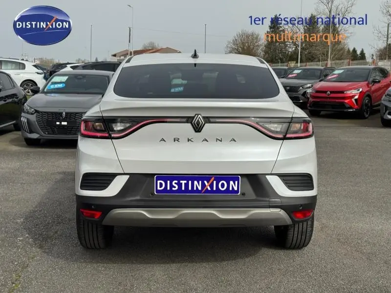 Vue arrière d'un Renault Arkana blanc 2025 avec feux reliés par un bandeau lumineux rouge, sur parking extérieur.