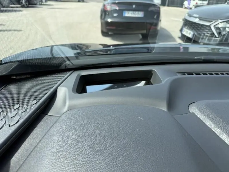 Vue intérieure du tableau de bord d'un Toyota C-HR Hybride 2024, avec pare-brise et véhicules en stationnement visibles à l'avant.
