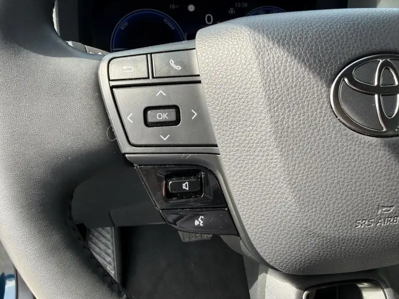 Gros plan sur le volant gris du Toyota C-HR Hybride 2024, avec commandes multifonctions et logo Toyota visible.