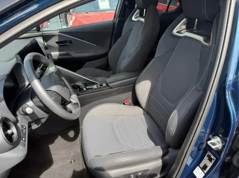 Vue intérieure côté conducteur du Toyota C-HR Hybride 2024 bleu persan, mettant en valeur les sièges sport et le tableau de bord moderne.