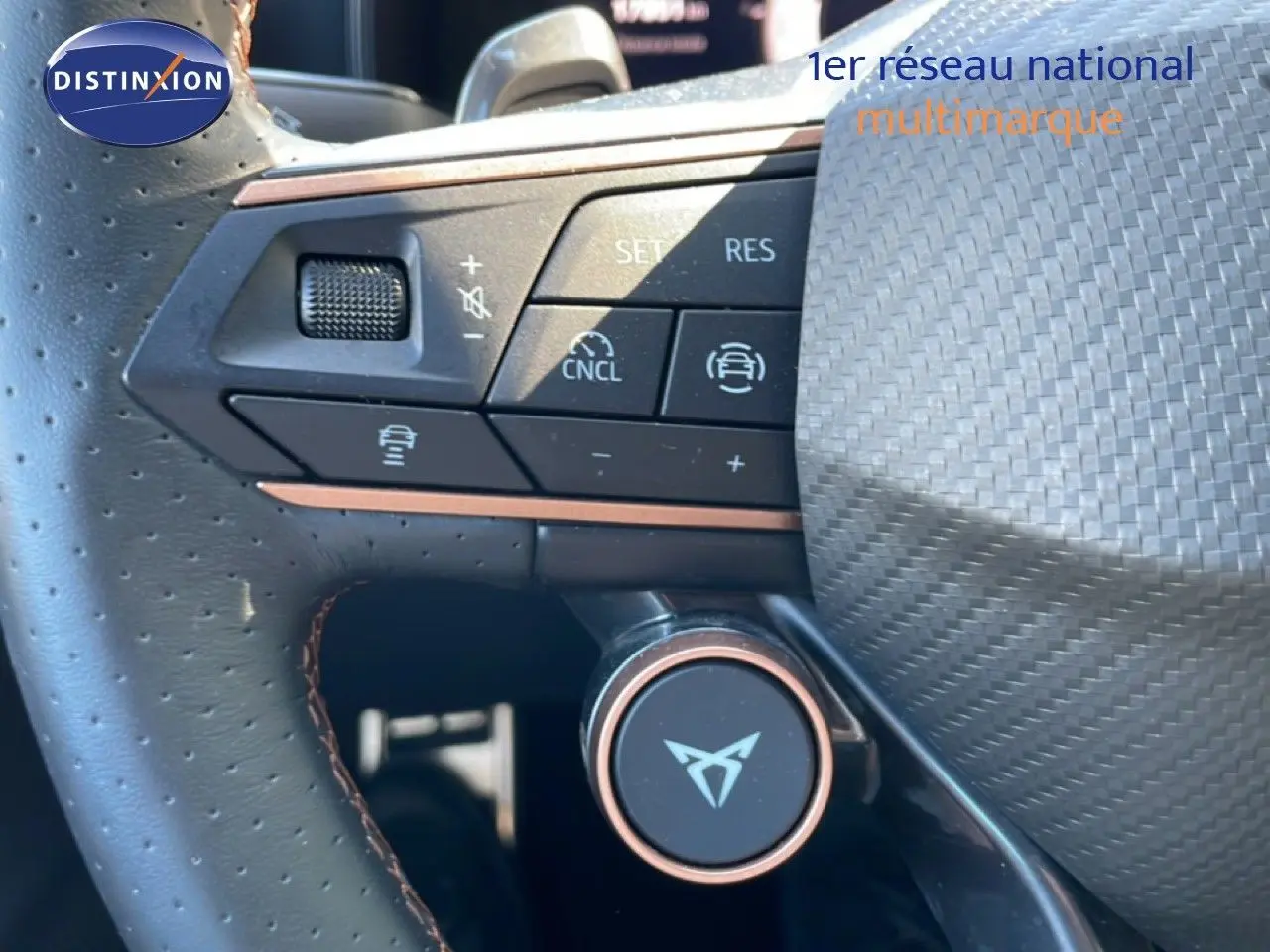 Gros plan sur le volant en cuir perforé avec commandes multifonctions et logo CUPRA au centre, intérieur noir.