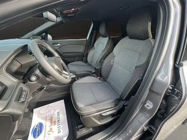 Vue intérieure côté conducteur du Renault Captur gris foncé 2025, sièges tissu gris et volant multifonctions cuir synthétique.