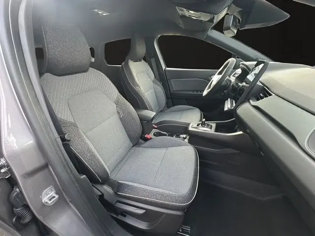 Vue intérieure côté gauche du Renault Captur 2025 gris foncé, montrant les sièges avant en tissu et le tableau de bord moderne.