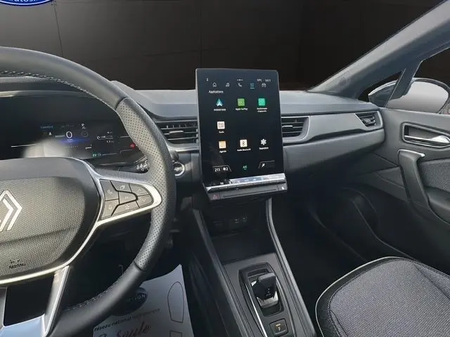 Vue intérieure côté conducteur du Renault Captur gris foncé 2025, avec écran tactile central vertical et volant multifonctions en cuir synthétique.