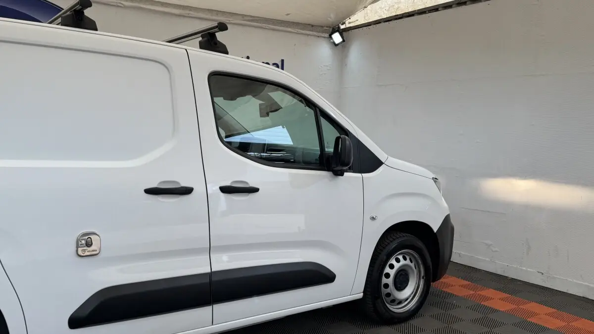 Vue latérale droite d’un Peugeot Partner blanc avec protections noires sur portes et jante acier simple.