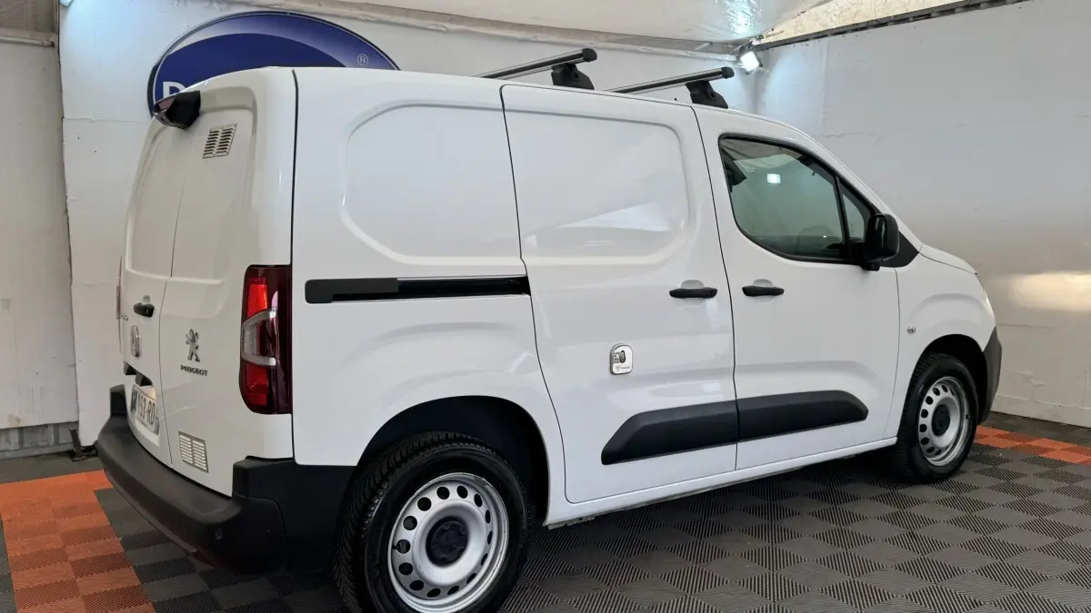 Vue 3/4 arrière droite d'un utilitaire Peugeot Partner blanc avec barres de toit et jantes acier.
