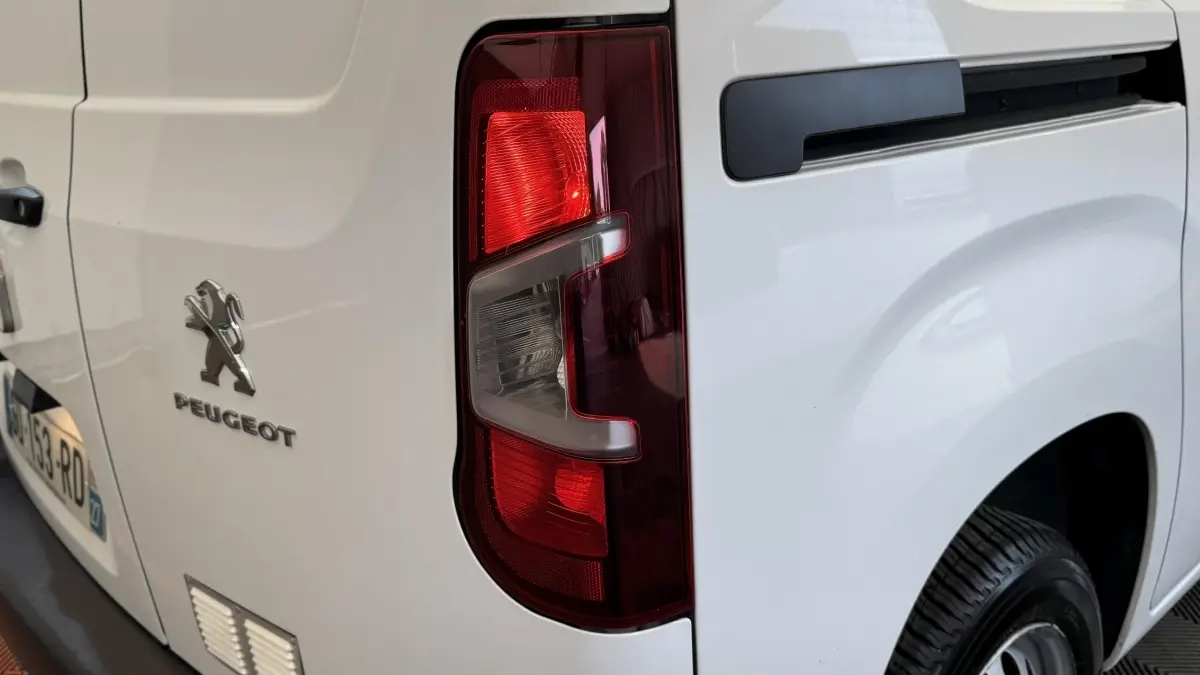 Vue arrière droite du Peugeot Partner blanc, mettant en valeur le feu arrière et le logo Peugeot sur la porte.