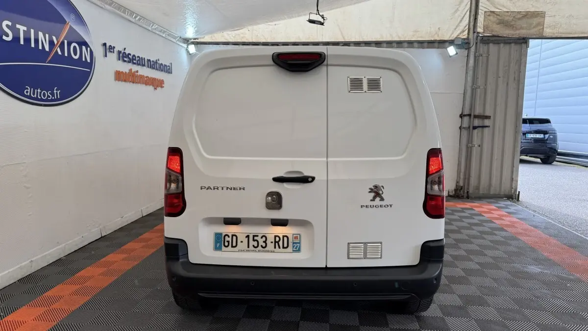 Vue arrière d’un utilitaire Peugeot Partner blanc avec feux arrière allumés et plaques d’immatriculation françaises.