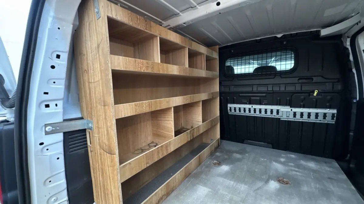 Intérieur arrière du Peugeot Partner blanc 2021, vue côté gauche montrant étagères en bois et cloison noire pleine.