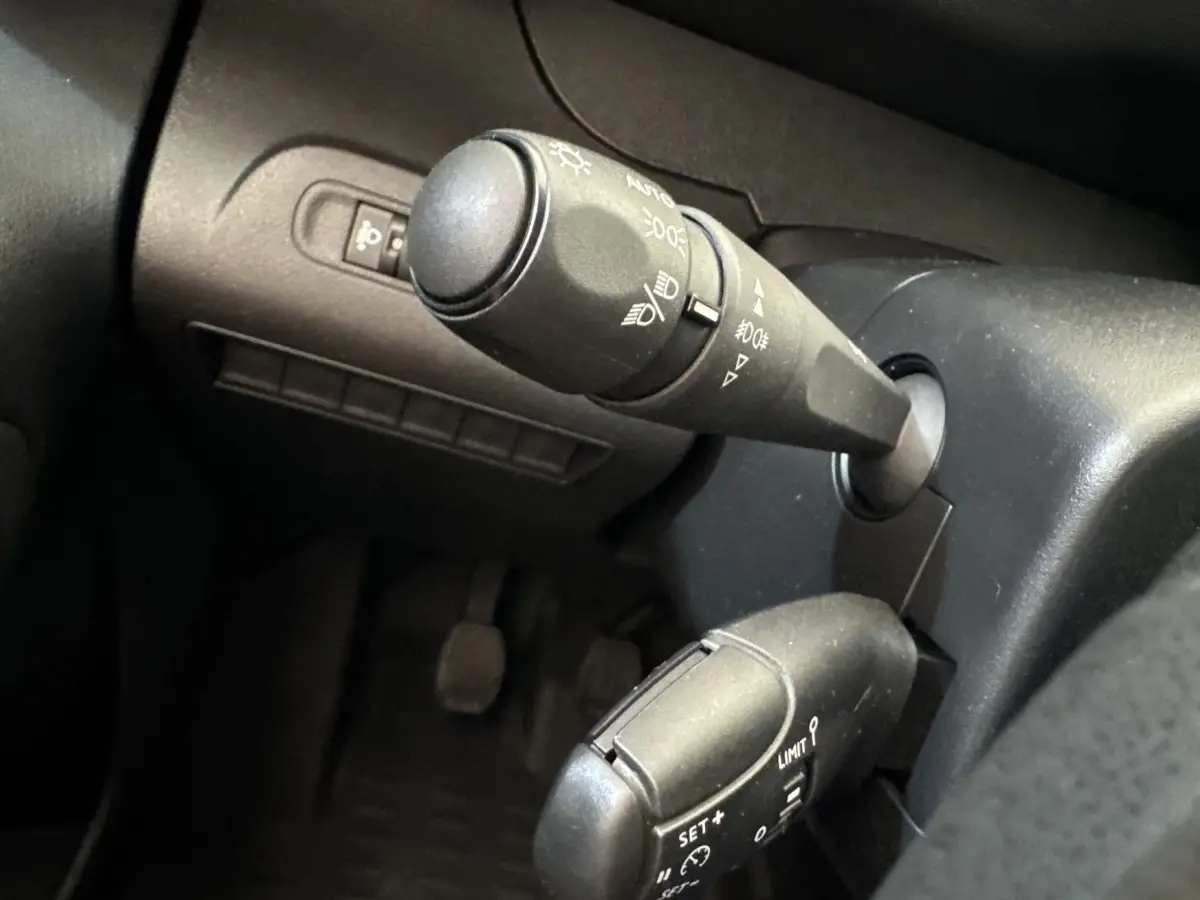 Gros plan sur les commandes de phares et régulateur de vitesse dans l'habitacle noir du Peugeot Partner 2021.