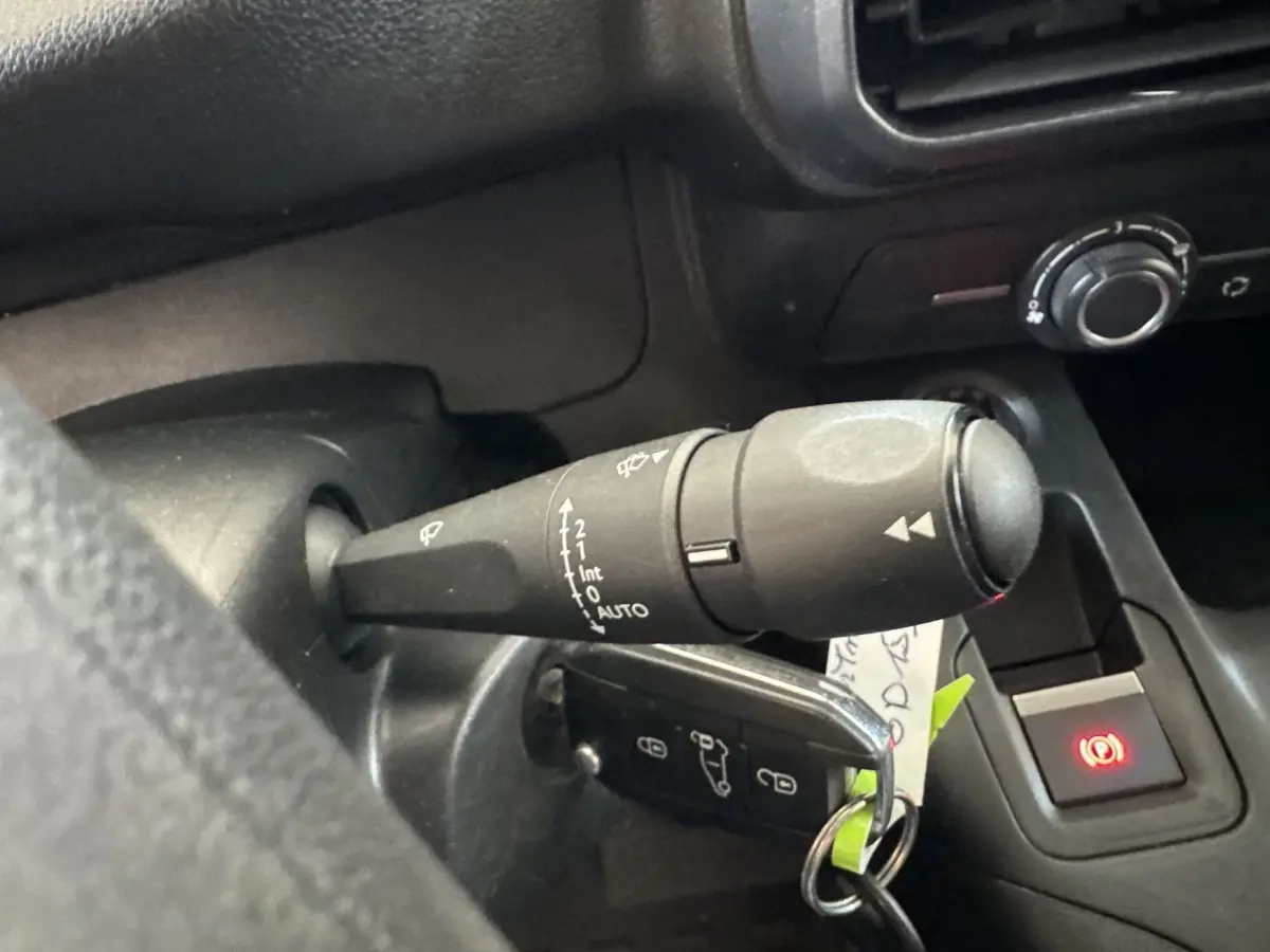 Gros plan sur la manette d’essuie-glace à gauche du volant dans l’habitacle noir du Peugeot Partner blanc.