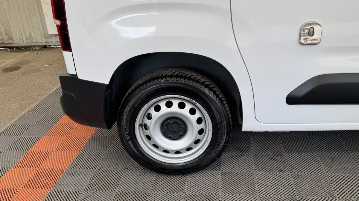 Gros plan sur la roue arrière droite acier d’un Peugeot Partner blanc avec pare-chocs noir et trappe latérale.