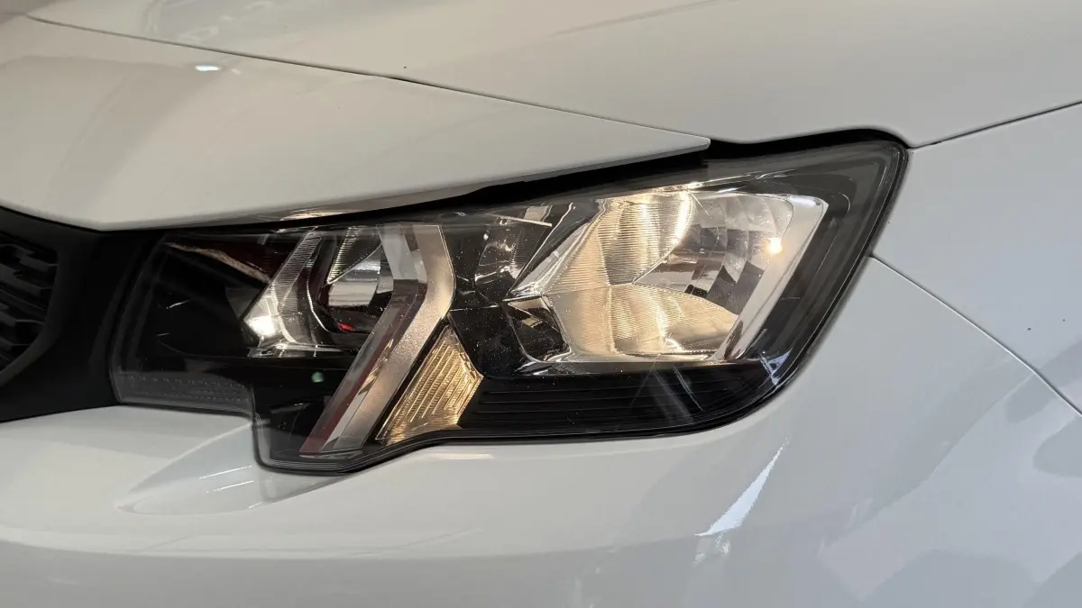 Gros plan sur le phare avant droit du Peugeot Partner blanc, mettant en valeur ses détails lumineux et la carrosserie.
