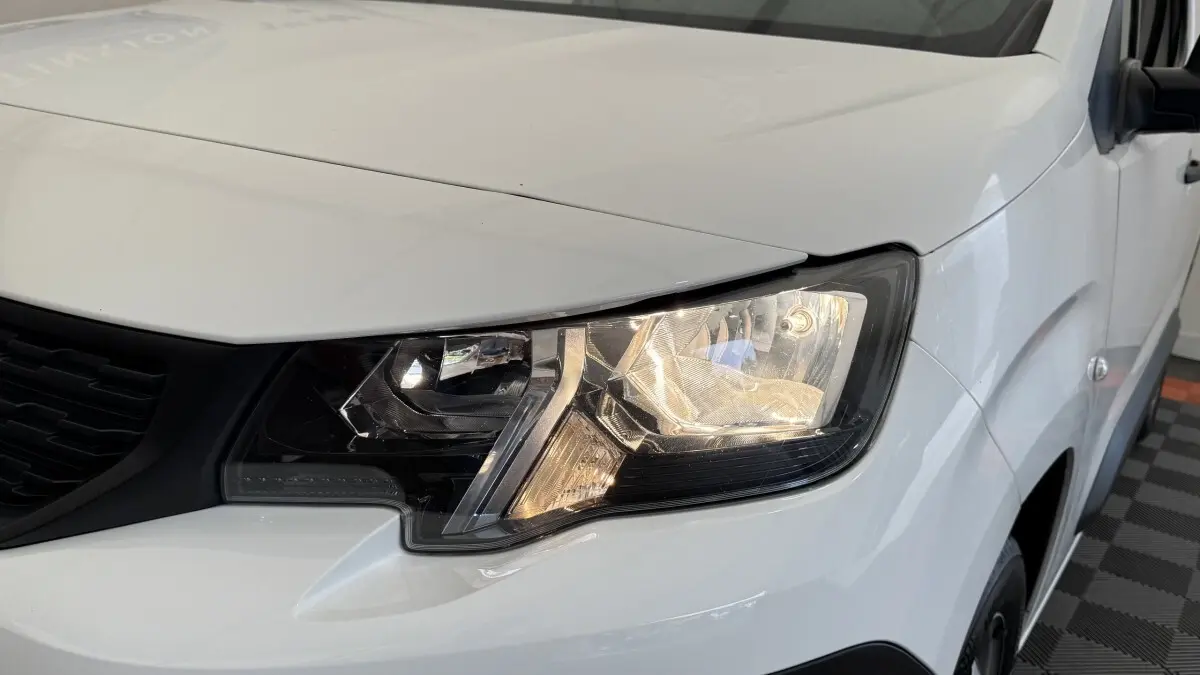 Gros plan sur le phare avant droit du Peugeot Partner blanc, mettant en valeur les détails du bloc optique.