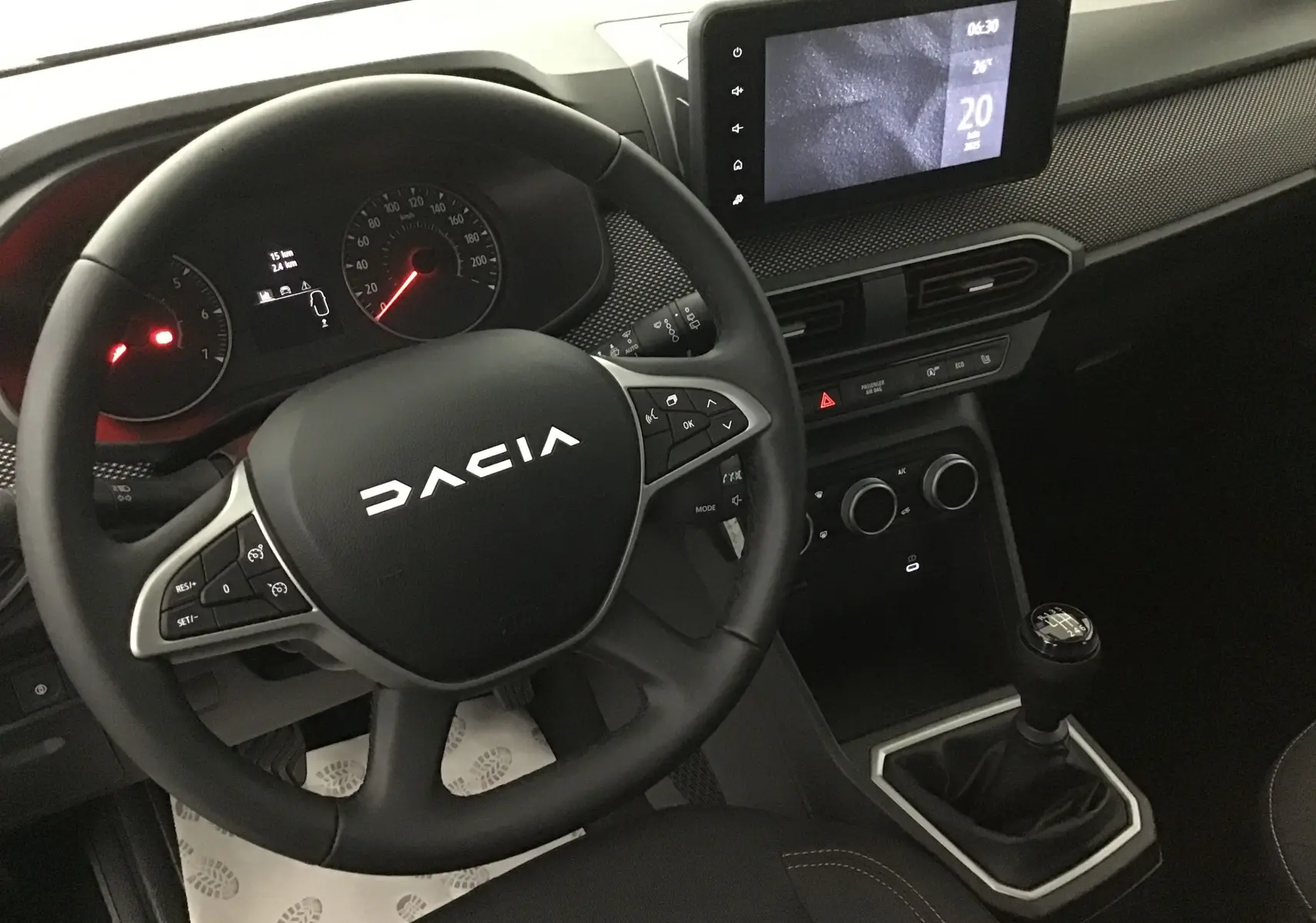 Vue intérieure centrée sur le volant DACIA et la console avec écran tactile et levier de vitesses manuelle.